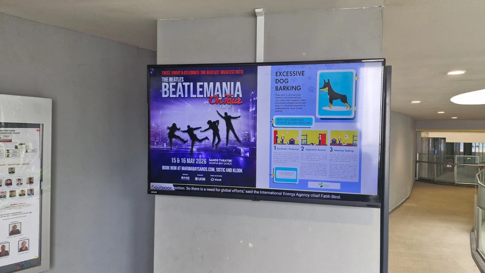 Digital advertising screen beside a condominium lobby door, with the swimming pool visible outside